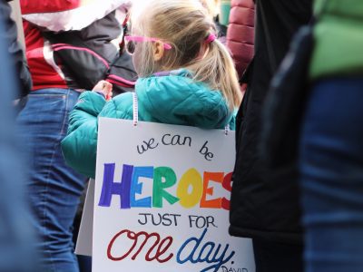 Child wearing a sign saying "We can be heroes by David Bowie"
