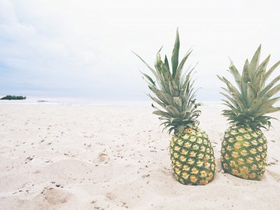 2 similar looking pineapples on a beach.