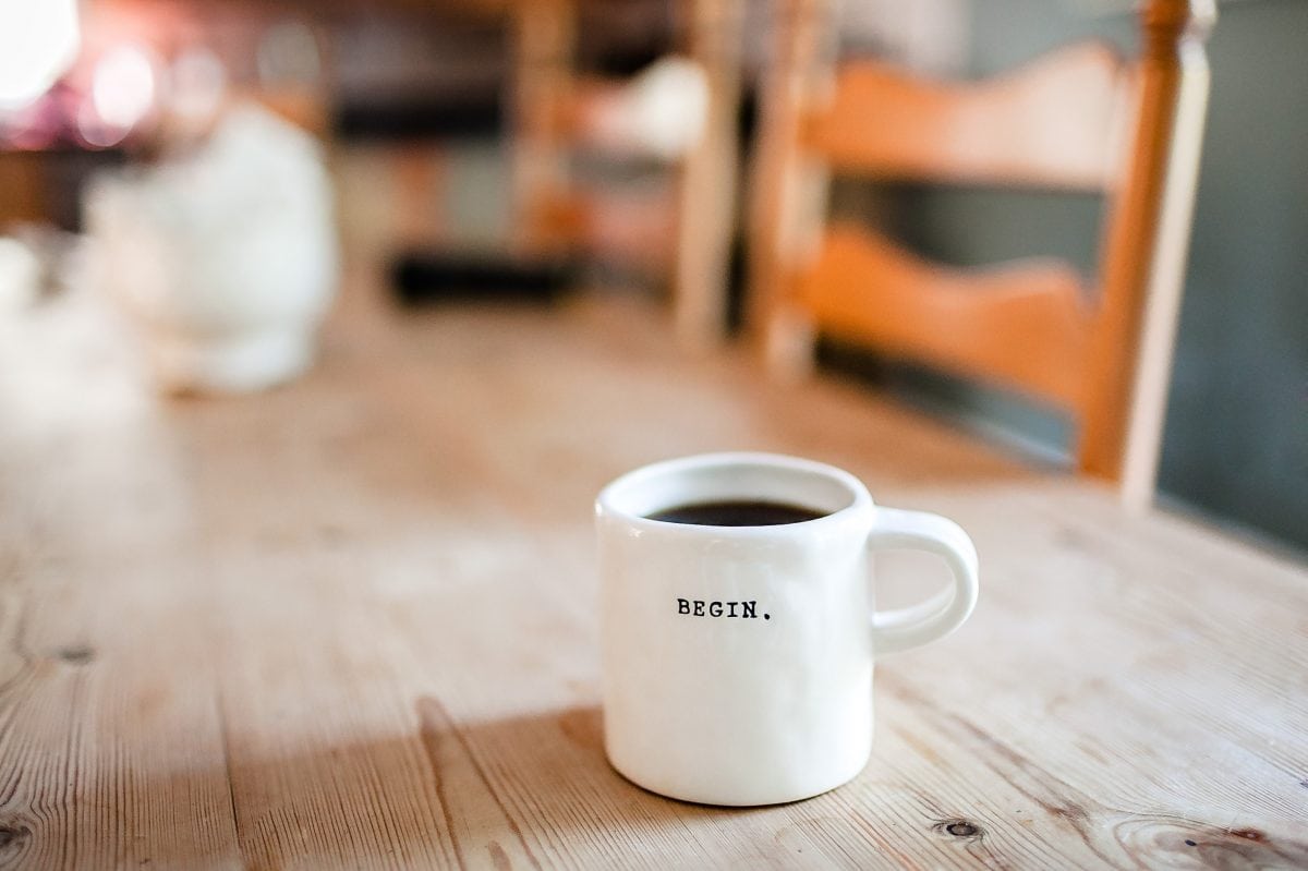 A white coffee mug with “begin” written on it on a wooden table