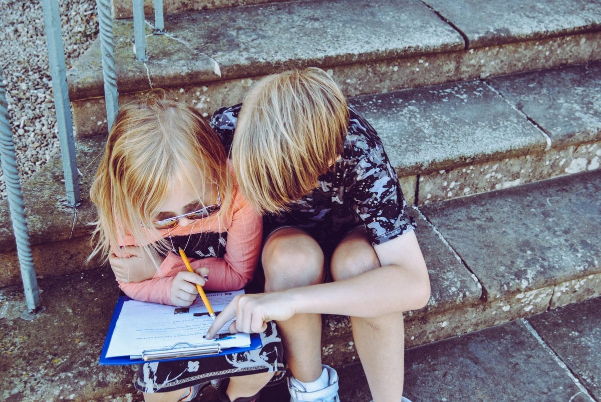 Two children writing on a piece of paper.