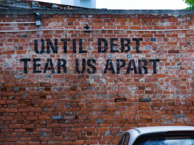 Brick wall with "until debt tear us apart" painted on it.