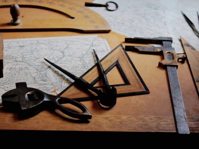 A map, protractor, and other old style measuring tools on a desk.
