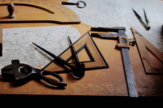 A map, protractor, and other old style measuring tools on a desk.