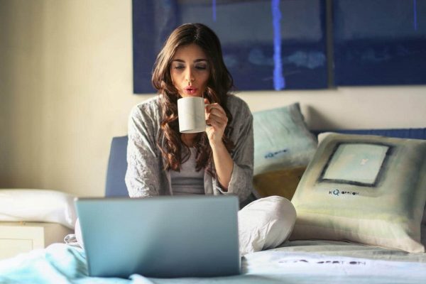 lady drinking coffee in bed while using a laptop