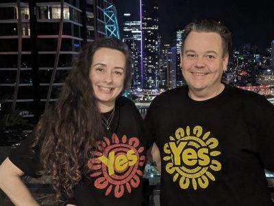 Elyse and Sam from Meeum wearing YES t-shirts with the Brisbane skyline in the background